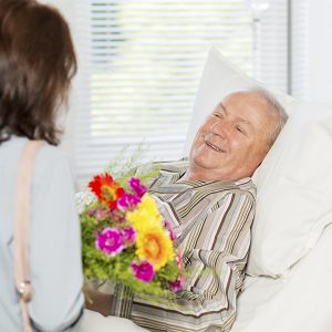 Senior man receiving flowers in hospital bed
