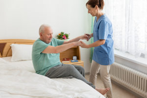 Caregiver helping a senior man get out of bed to avoid pressure sores