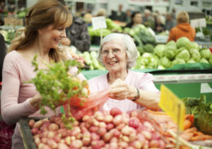 A caregiver helps an older adult grocery shop to avoid senior dietary problems.