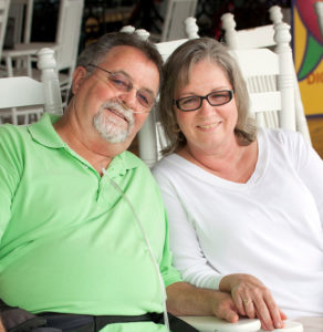 A mature couple sit on rocking chairs, implementing tips to breathe easier with lung disease by conserving energy.