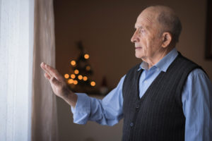 An older man looks out the window and waves goodbye to his family. During the holidays, families should look for any signs of seasonal affective disorder in older loved ones.