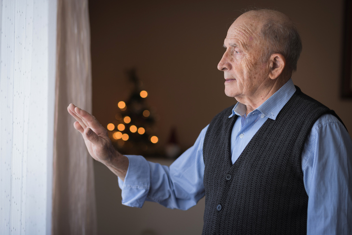 An older man looks out the window and waves goodbye to his family. During the holidays, families should look for any signs of seasonal affective disorder in older loved ones.