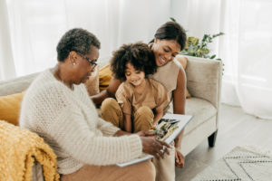 An older woman sits on a couch and looks through a book with her daughter and grandchild, leaving a legacy of what matters to future generations.