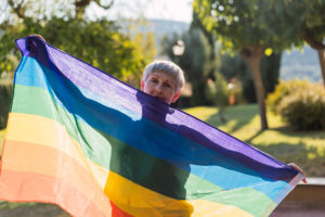 An older woman proudly supports LGBTQ+ seniors by holding up a rainbow flag.