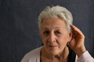 An older woman with hearing loss cups her ear to hear.