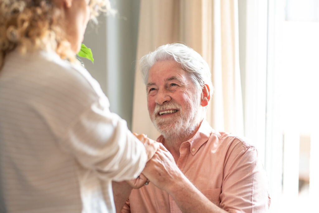 A man undergoing stroke recovery at home holds the hands of his caregiver.
