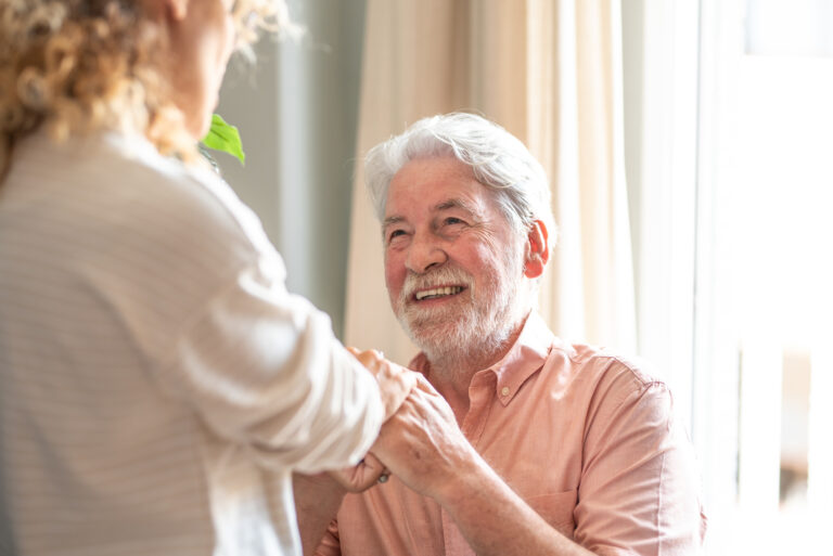 A man undergoing stroke recovery at home holds the hands of his caregiver.