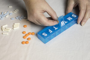 Hands place medications into a pill box, one way to improve medication schedules for seniors.