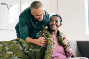 A man who has learned how to prevent mistakes when caring for someone with Alzheimer’s wraps a blanket around an older woman.