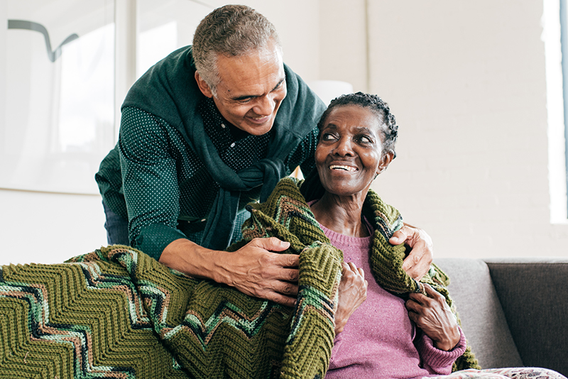 A man who has learned how to prevent mistakes when caring for someone with Alzheimer’s wraps a blanket around an older woman.