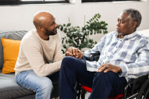 A man holds his dad’s hand and comforts him to ease the agitation of dementia behavior triggers.