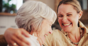 A caregiver laughs with an older woman as she incorporates techniques to improve mental health in seniors.
