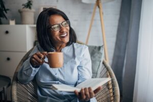 A woman who knows the importance of caring for yourself as a caregiver reads a book while enjoying a cup of coffee.