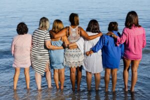 A group of women stand facing the ocean, supporting each other in caregiver burnout prevention.